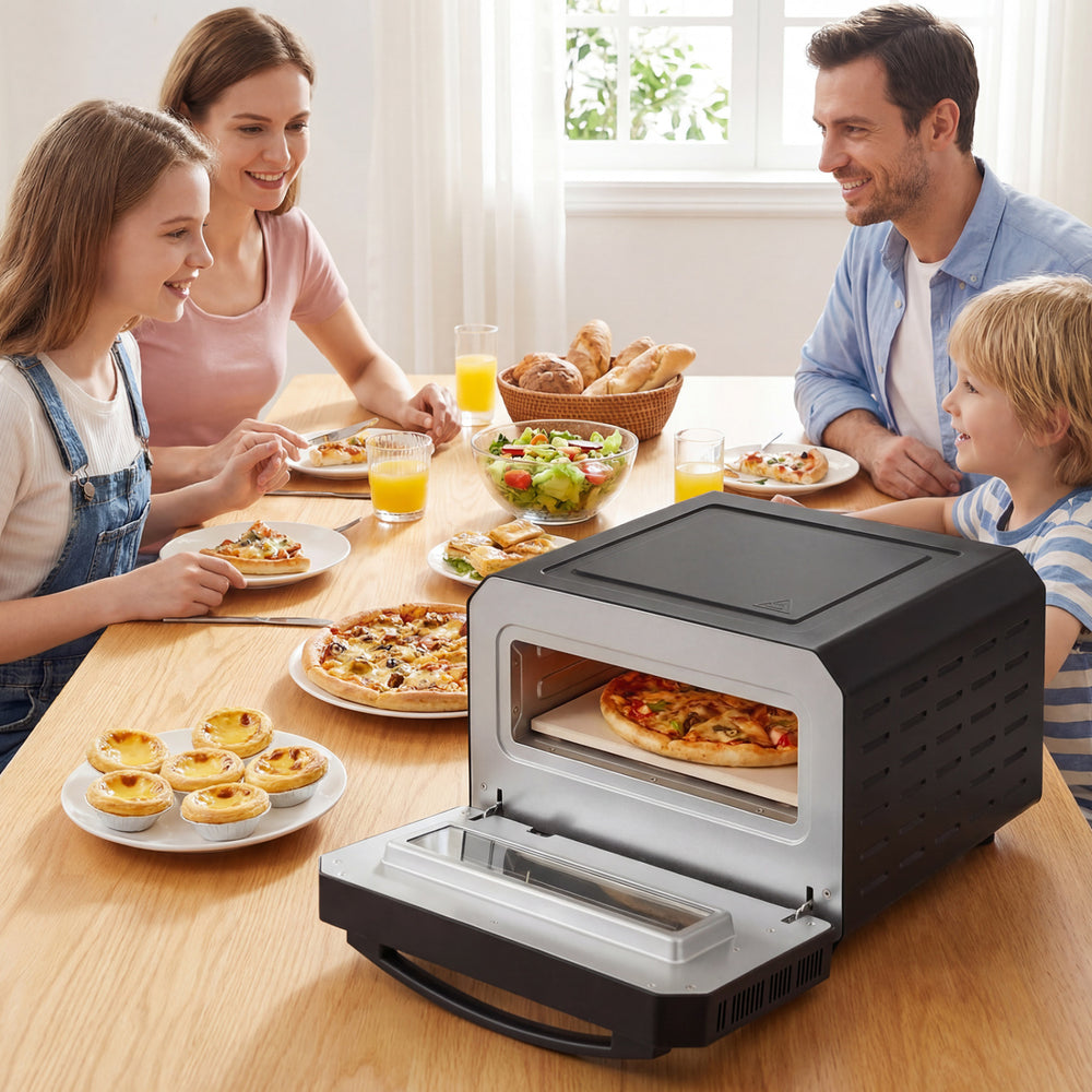 Indoor electric pizza oven in black, cooking 12-inch pizzas with a glass window, shown at a family meal setting.