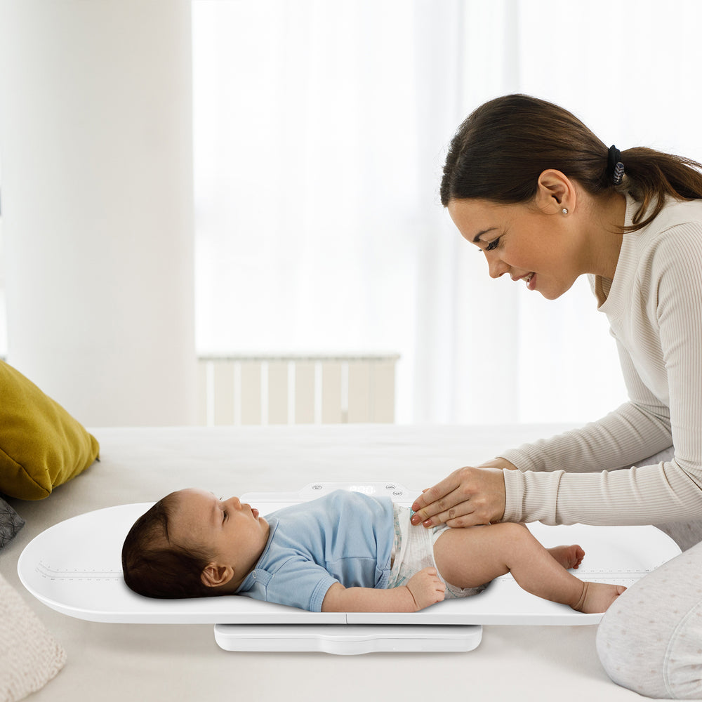 Infant scale with detachable tray, measuring weight and height, shown in use with a baby for growth tracking.
