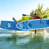 Two people carrying an inflatable stand-up paddle board with a stylish coco motif, ideal for all-skill levels on water.