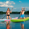 Two people paddling on inflatable stand-up paddle boards in vibrant colors on a calm lake, perfect for all skill levels.