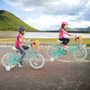 Two kids riding a green 16-inch bike with training wheels and front basket, perfect for outdoor fun and balance.