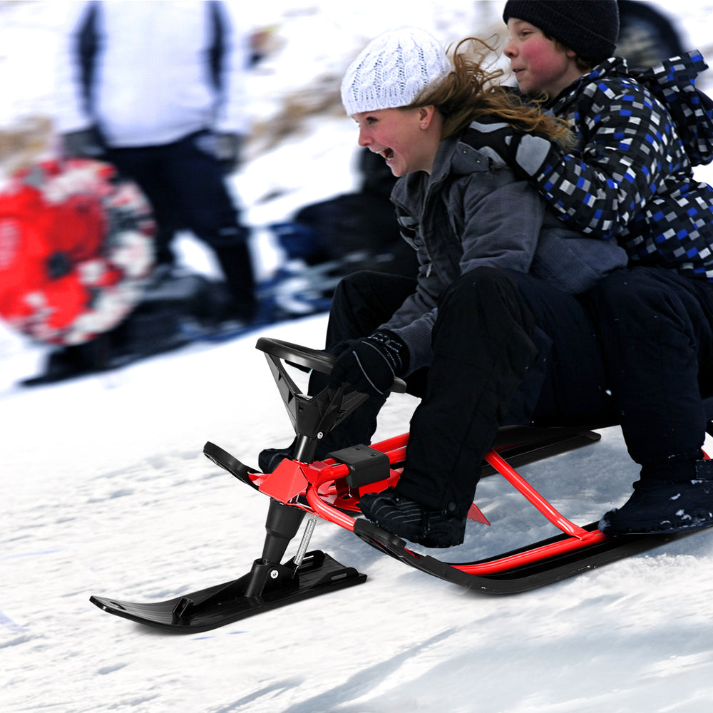 Kids snow sled in red with steering wheel and double brakes, designed for stability and control on snowy hills.