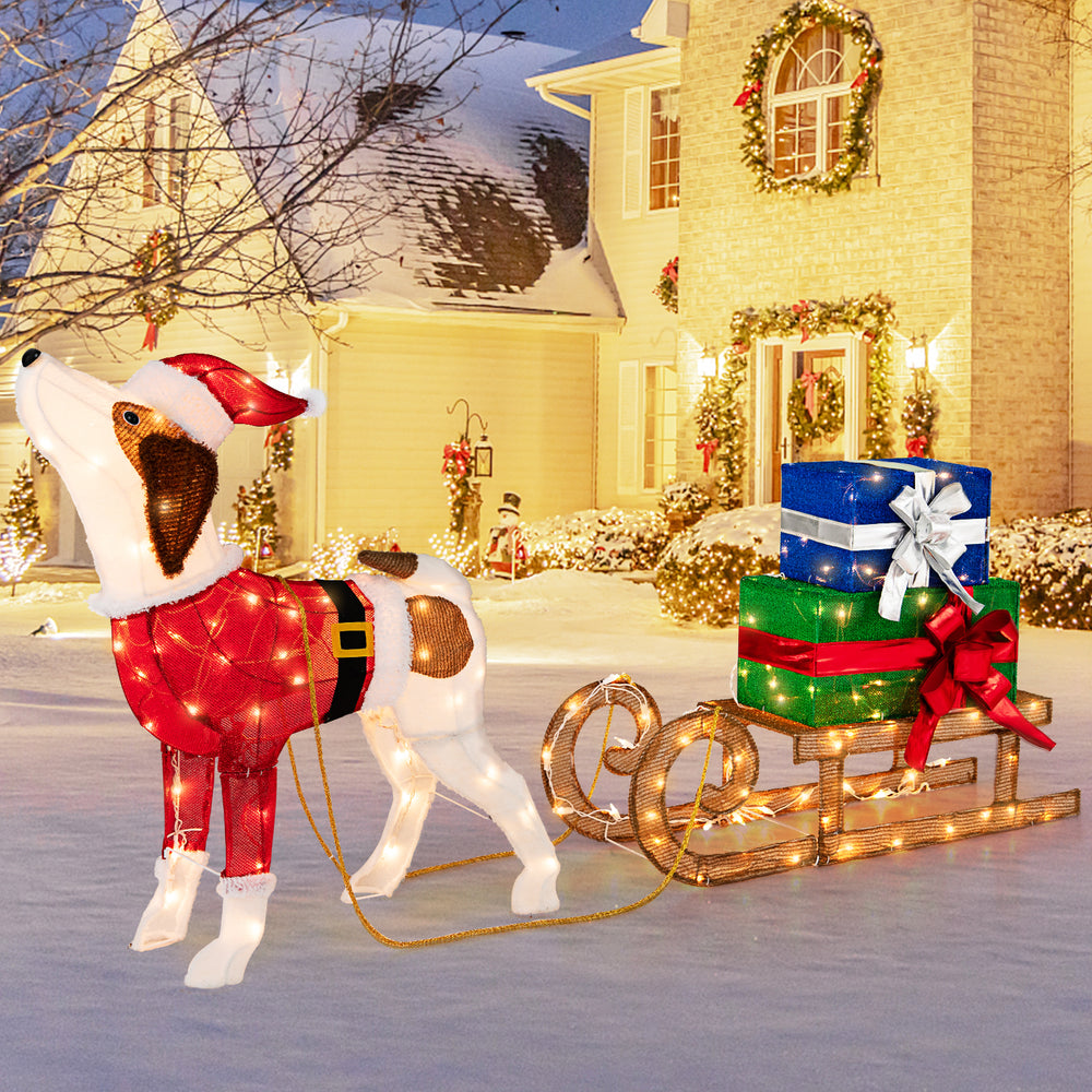 Pre-lit outdoor Xmas dog in a Santa outfit pulling a sleigh with gifts, ideal for festive porch decoration.