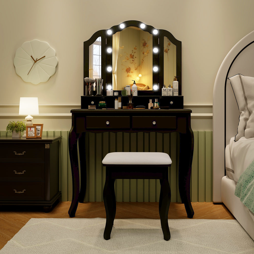 Makeup vanity table set in black with lighted tri-fold mirror, cushioned stool, and spacious storage for beauty.