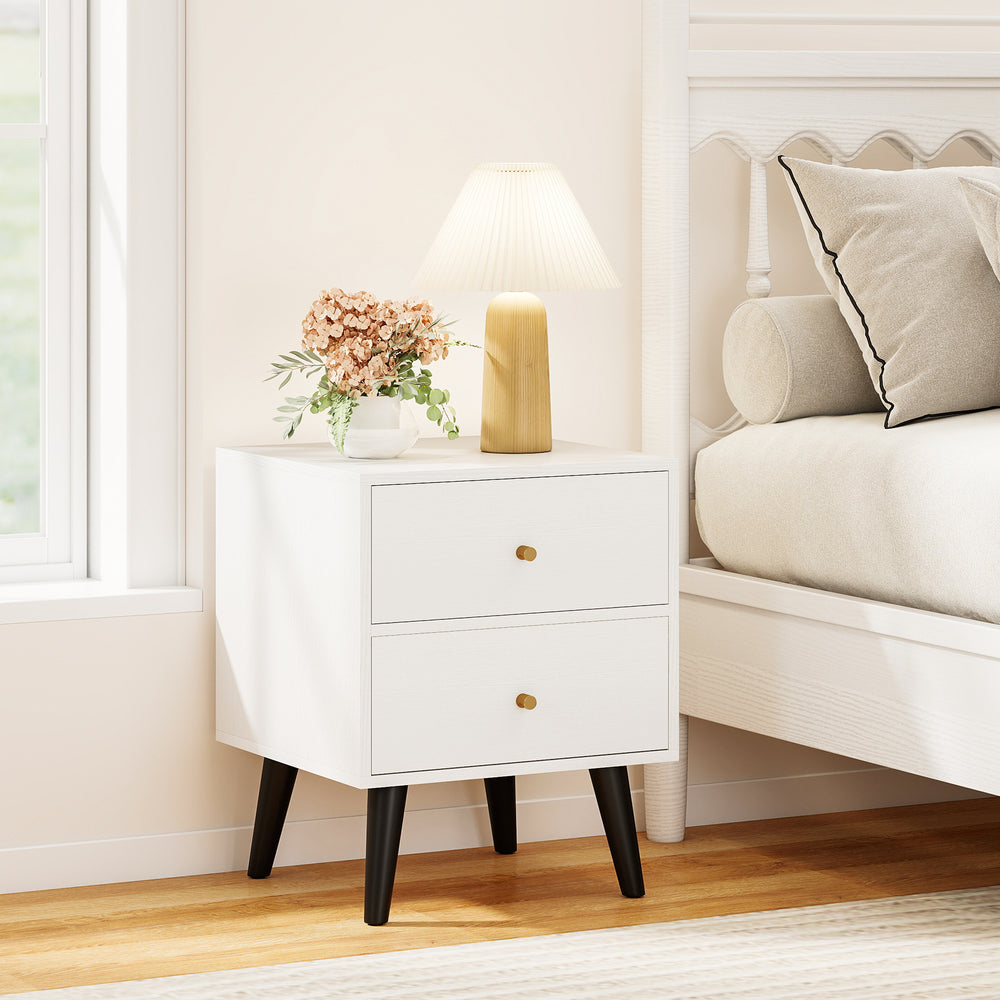 Mid Century Modern bedside table in white with golden knobs, featuring two drawers and tapered support legs for stylish.