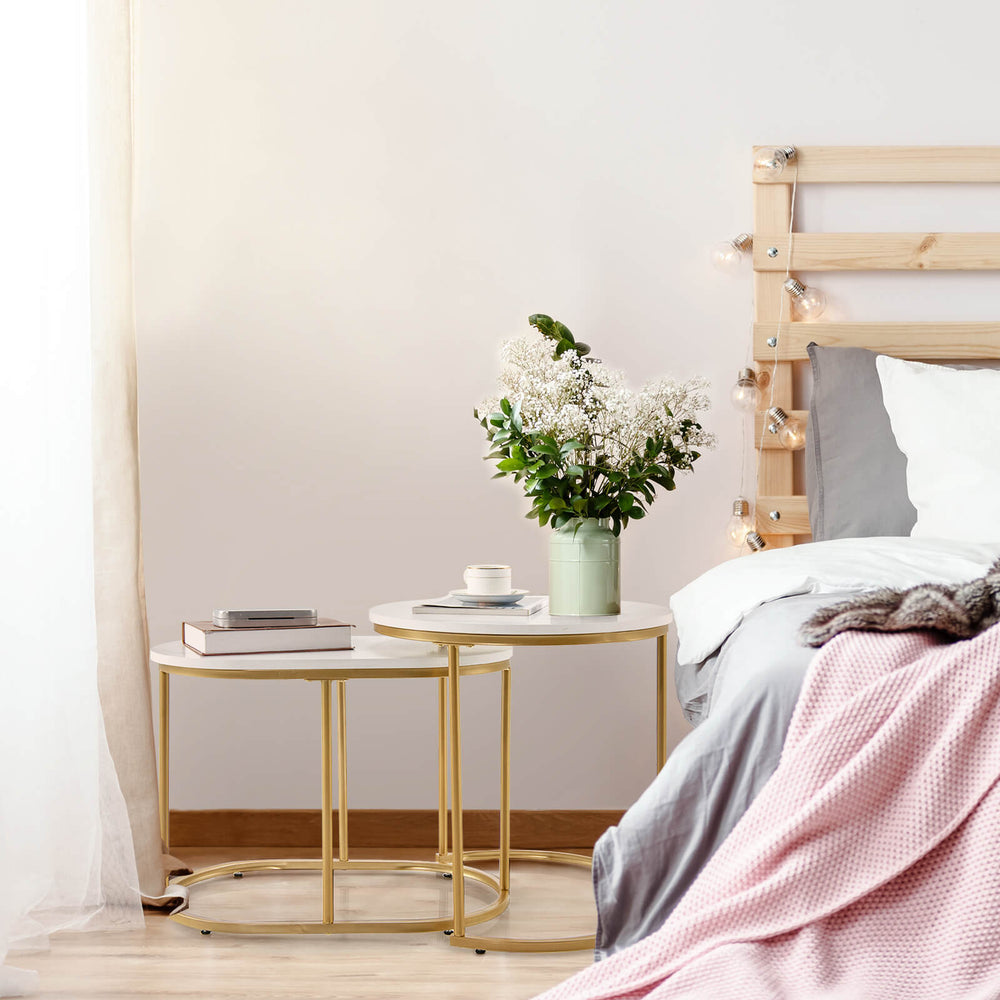 Nesting coffee tables set of 2 with white tops and gold frames, elegantly arranged beside a bed for versatile use.