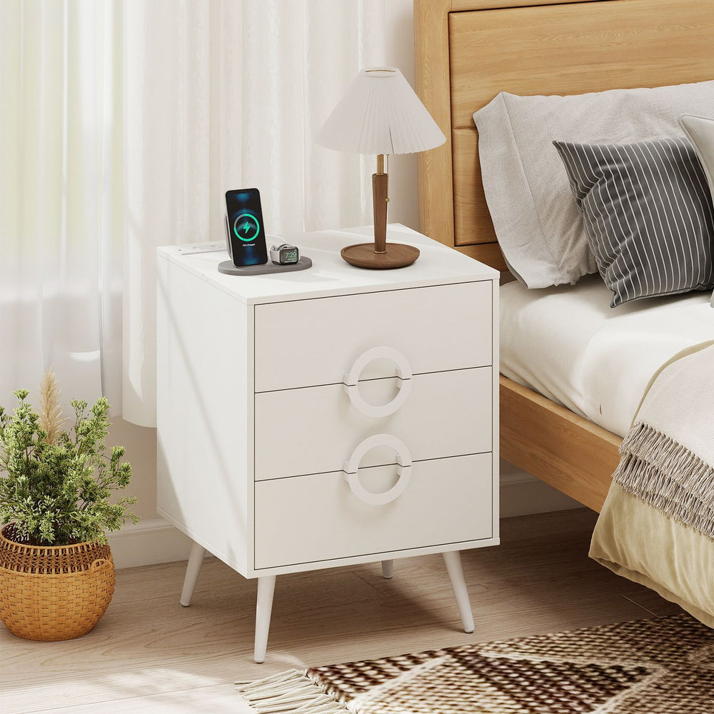 Modern white nightstand with three drawers, power outlets, and cable hole for organized charging beside the bed.