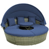 Round outdoor daybed with retractable canopy and navy cushions, featuring hand-woven PE wicker for patio relaxation.
