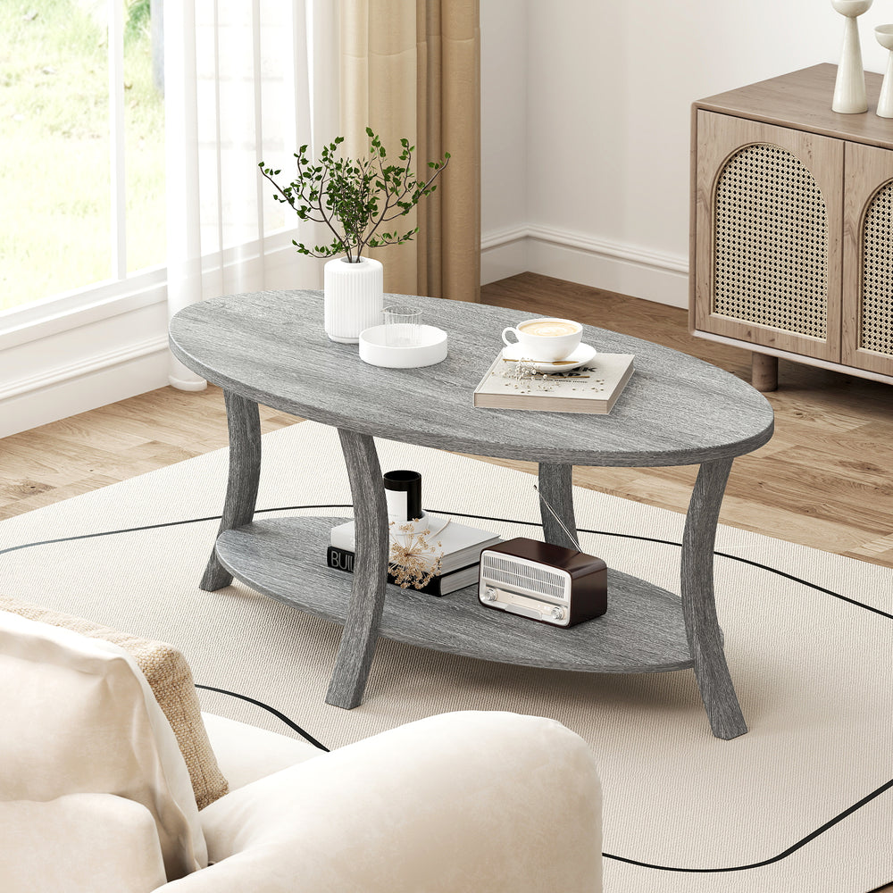 Gray oval coffee table with splayed support legs and open shelf, ideal for magazines and remote controls in any room.