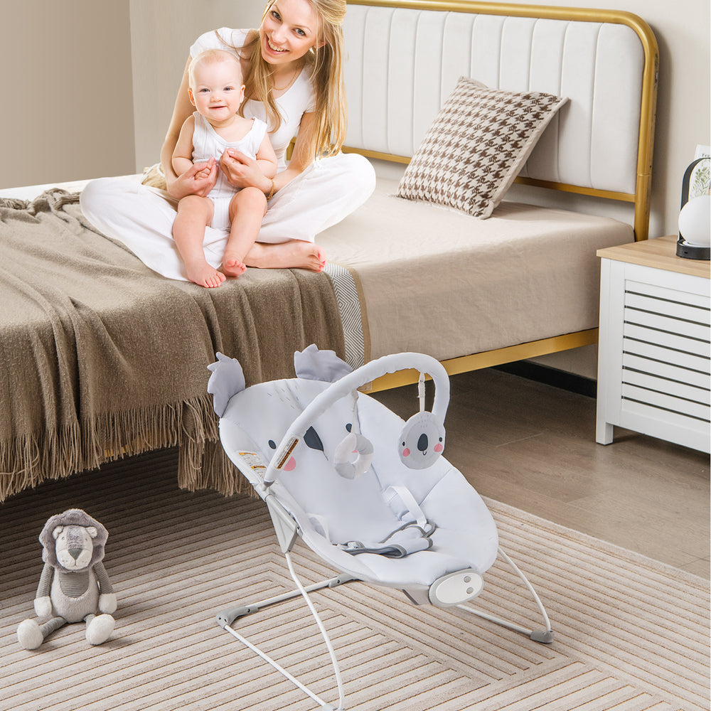 Portable gray baby bouncer with detachable toy bar, ergonomic design, and safety harness for infant comfort and play.