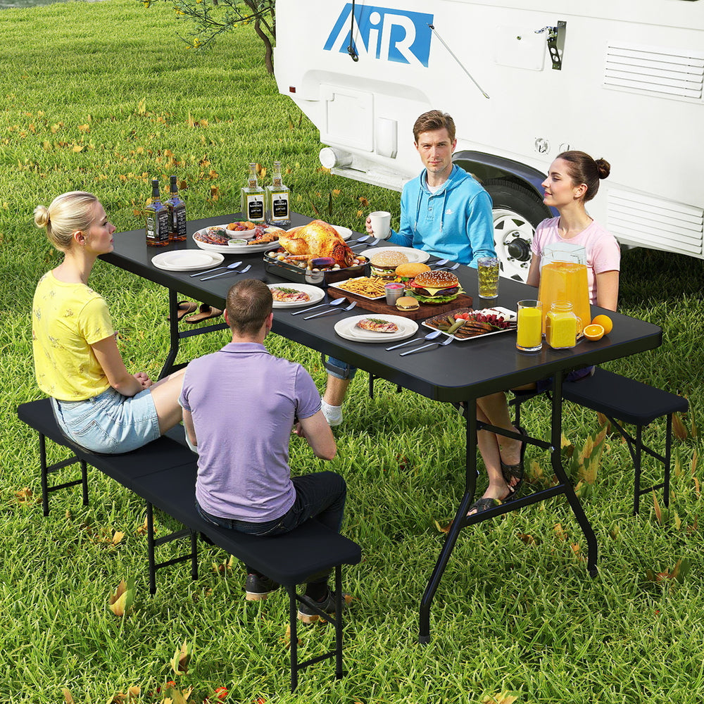 Portable folding camping table with a large black tabletop, set up for a picnic, accommodating food and drinks.