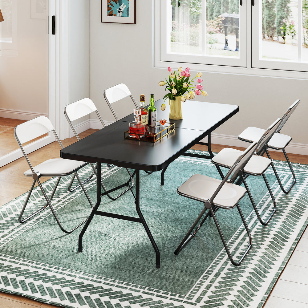 Portable black folding camping table with sturdy steel frame, set up for dining, surrounded by six white folding chairs.