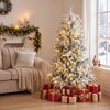 Pre-lit artificial Christmas tree with warm white LED lights, snow flocking, and festive gifts for a cozy holiday display.