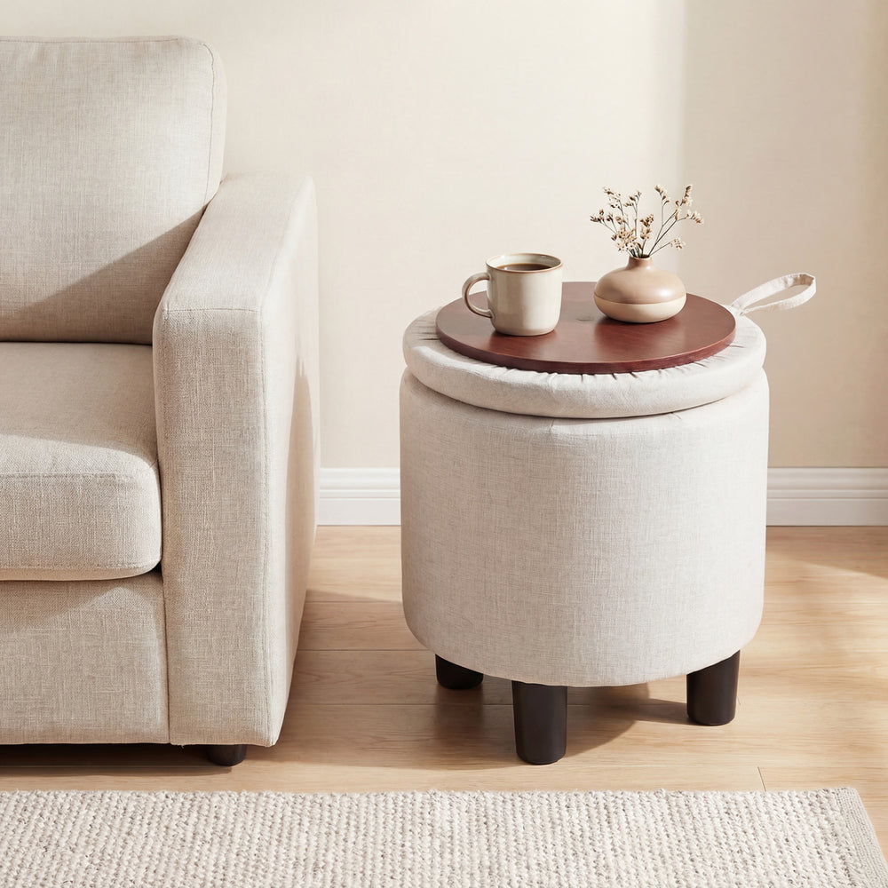 Beige round storage ottoman with removable lid, serving as a footrest and side table, perfect for modern living rooms.