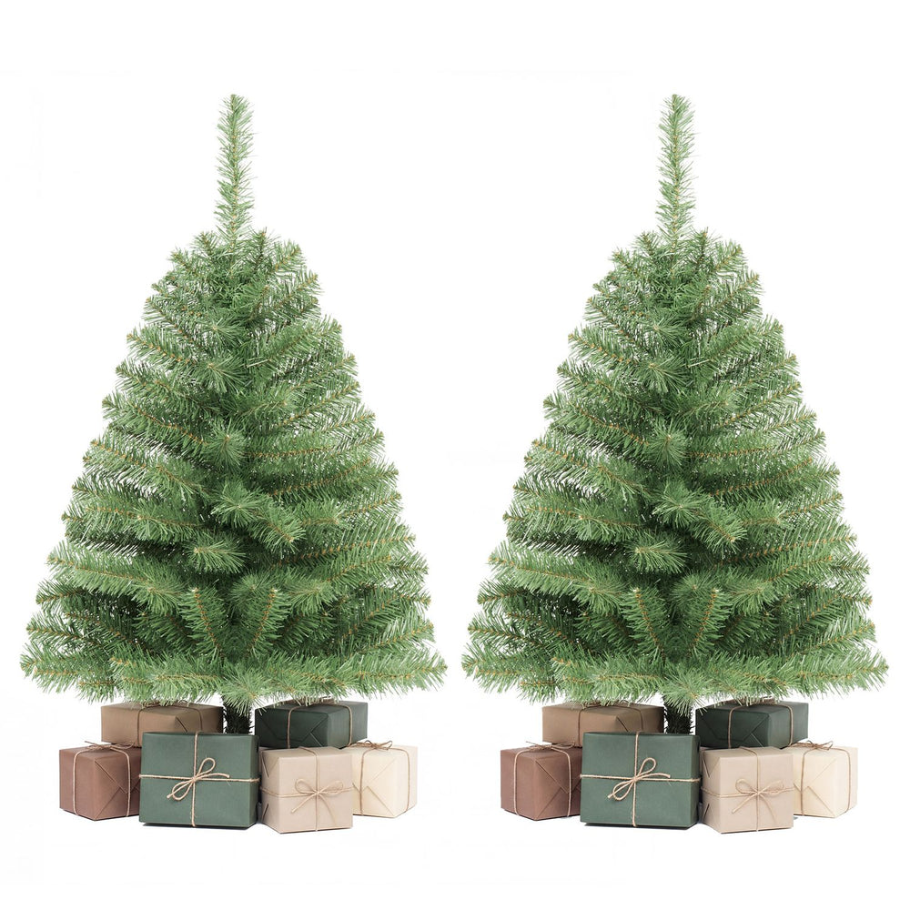 Two 3 FT mini tabletop Christmas trees with 113 green PVC branch tips stand beside wrapped gifts.