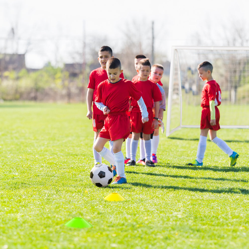 Youth soccer players practice with a ball near a weather-resistant 8' x 6' soccer goal and colorful training cones.