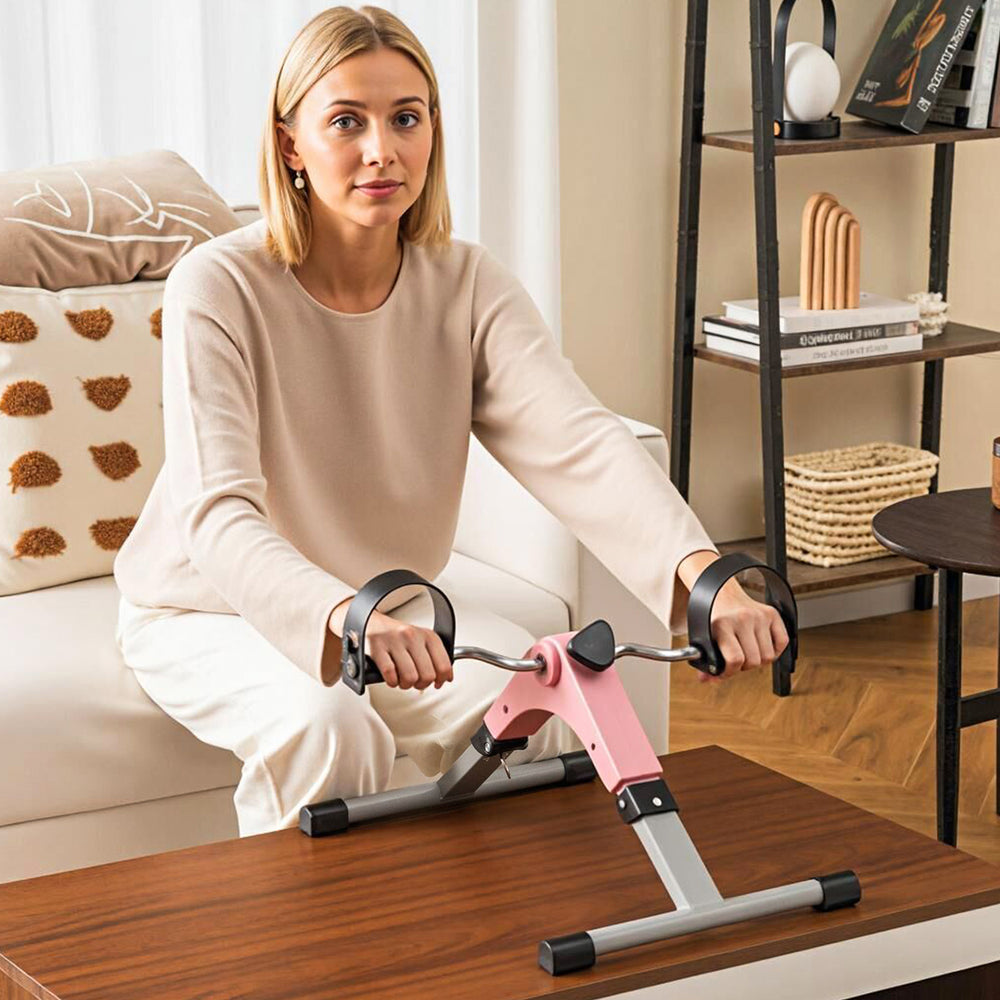 Under desk exercise bike pedal exerciser in pink, designed for arms and legs workout with adjustable resistance and LCD.