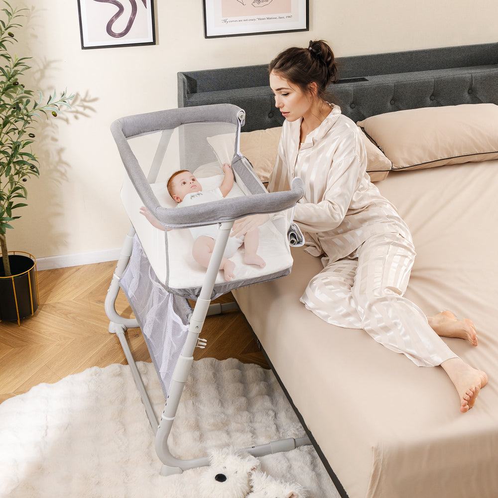Baby bassinet bedside crib in gray with adjustable height, mesh sides, and comfy mattress for easy access to baby.