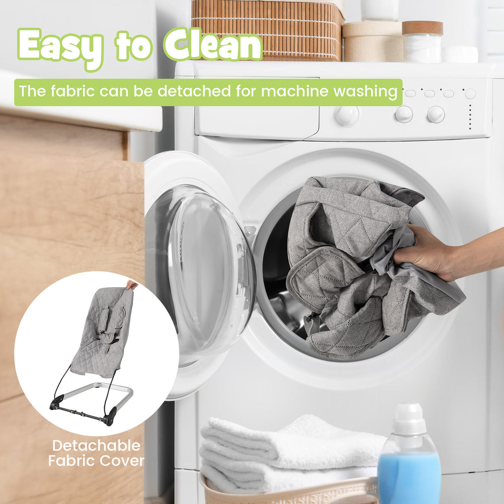 Light gray baby bouncer seat with detachable fabric cover being placed in a washing machine for easy cleaning.