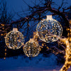 Three decorative Christmas LED light balls in different sizes, featuring warm and white lights, hung on a snowy tree.