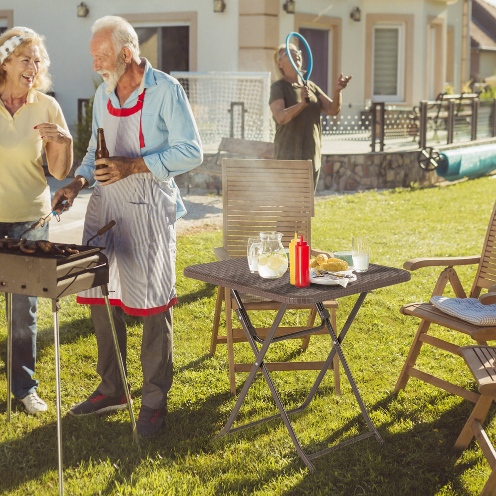 Folding picnic table featuring a rattan grain HDPE tabletop, set up for a backyard barbecue with food and drinks.
