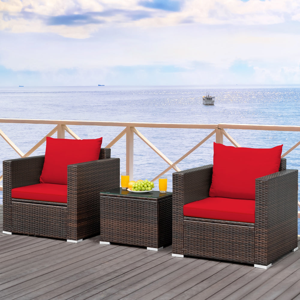 Two red-cushioned rattan chairs with a glass-top table, perfect for outdoor patio relaxation.