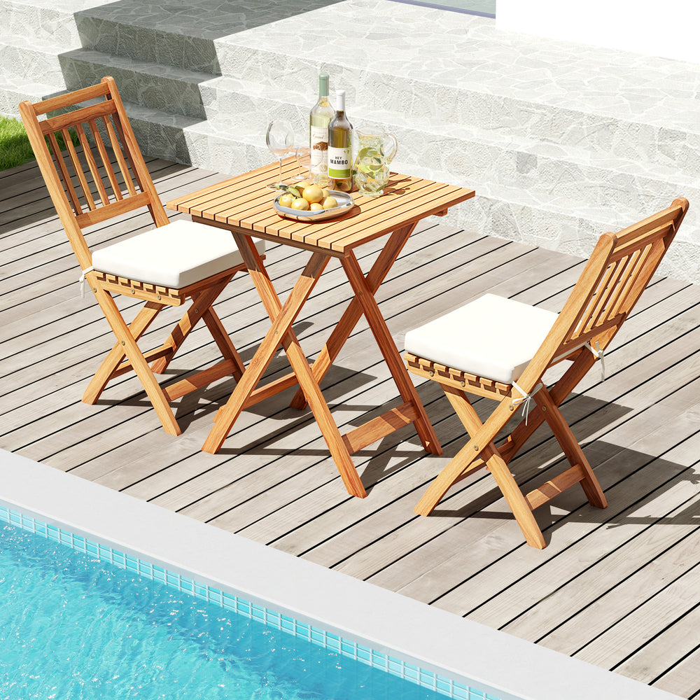 Outdoor wood bistro set featuring a folding table and two chairs with soft cushions, ideal for poolside relaxation.