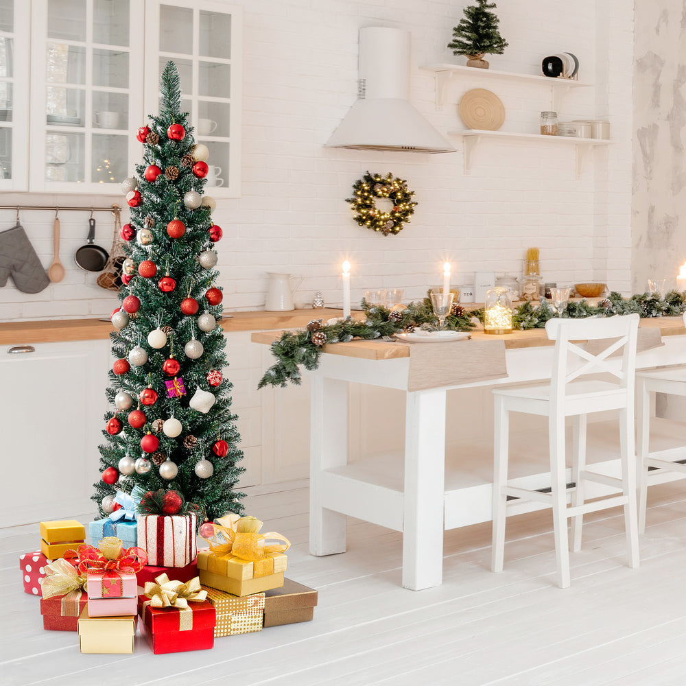 Snowy artificial pencil Christmas tree with pine cones, 5 ft tall, decorated with ornaments and surrounded by festive.