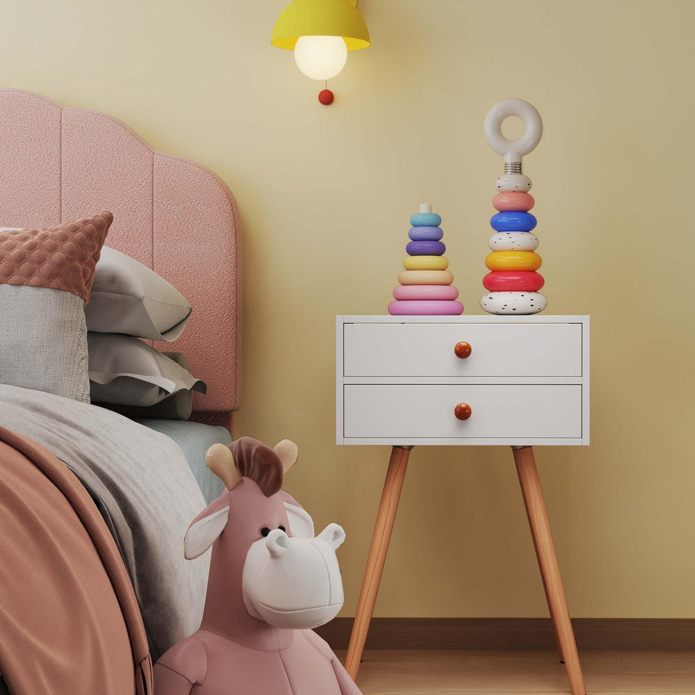 White storage end table with two drawers beside a pink twin bed and colorful stacking toy in a children's room.