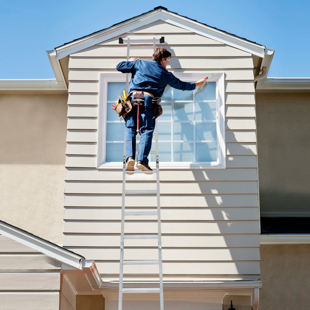 Folding aluminum ladder in use for window cleaning, featuring anti-slip rungs and safe locking hinge for stability.