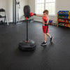 Child practicing boxing with an adjustable height punching bag and red gloves on a durable interlocking exercise mat.