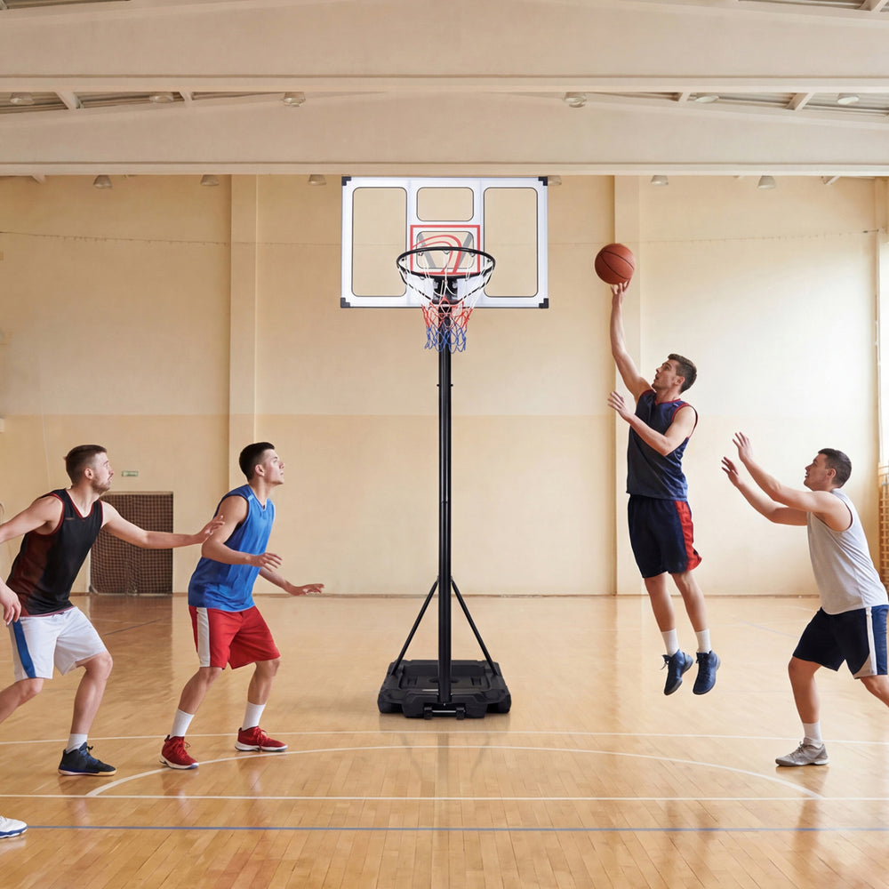 Adjustable portable basketball hoop with shatterproof backboard, shown in use by players in a gym setting.