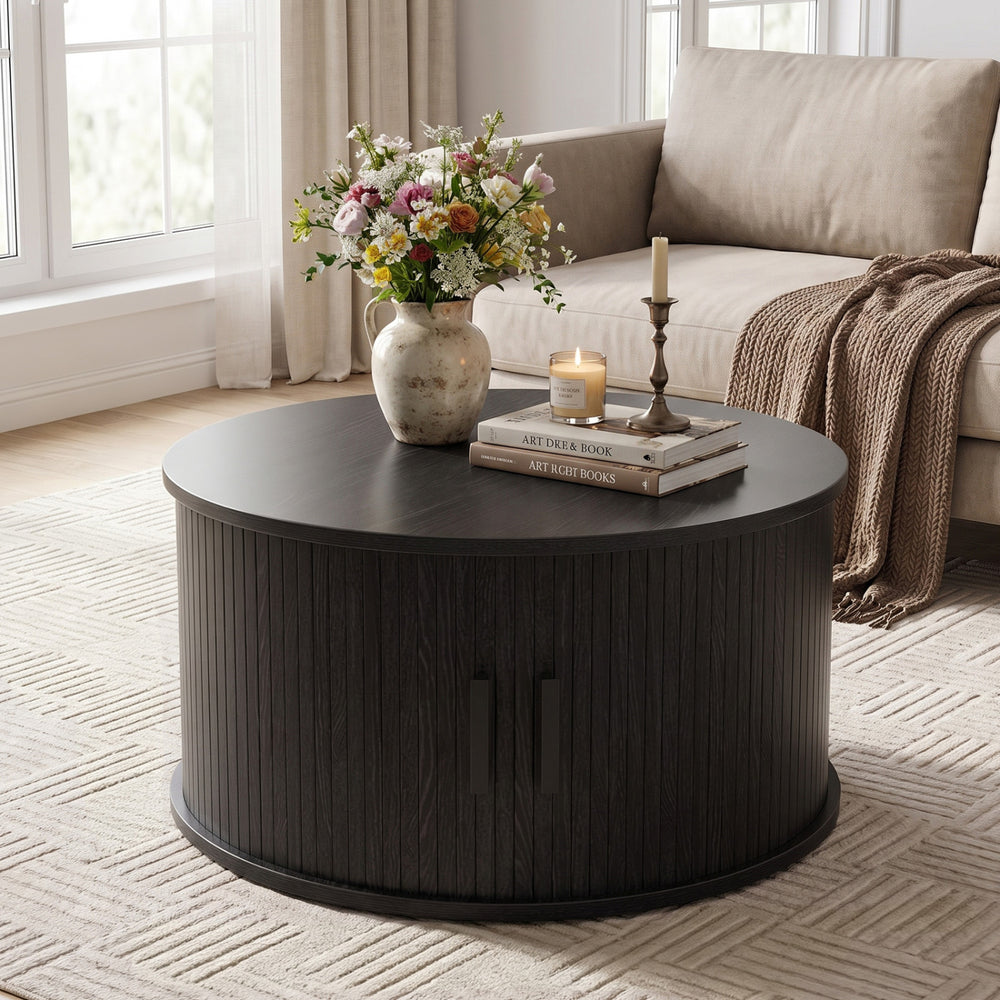 Round black coffee table with storage, featuring a fluted design and sliding tambour door for organized living room use.