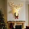 3D Rudolph hanging wreath with LED warm white lights, tinsel antlers and red bow above a Christmas mantel.